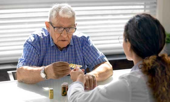 Image of man taking medication sitting across from a healthcare professional